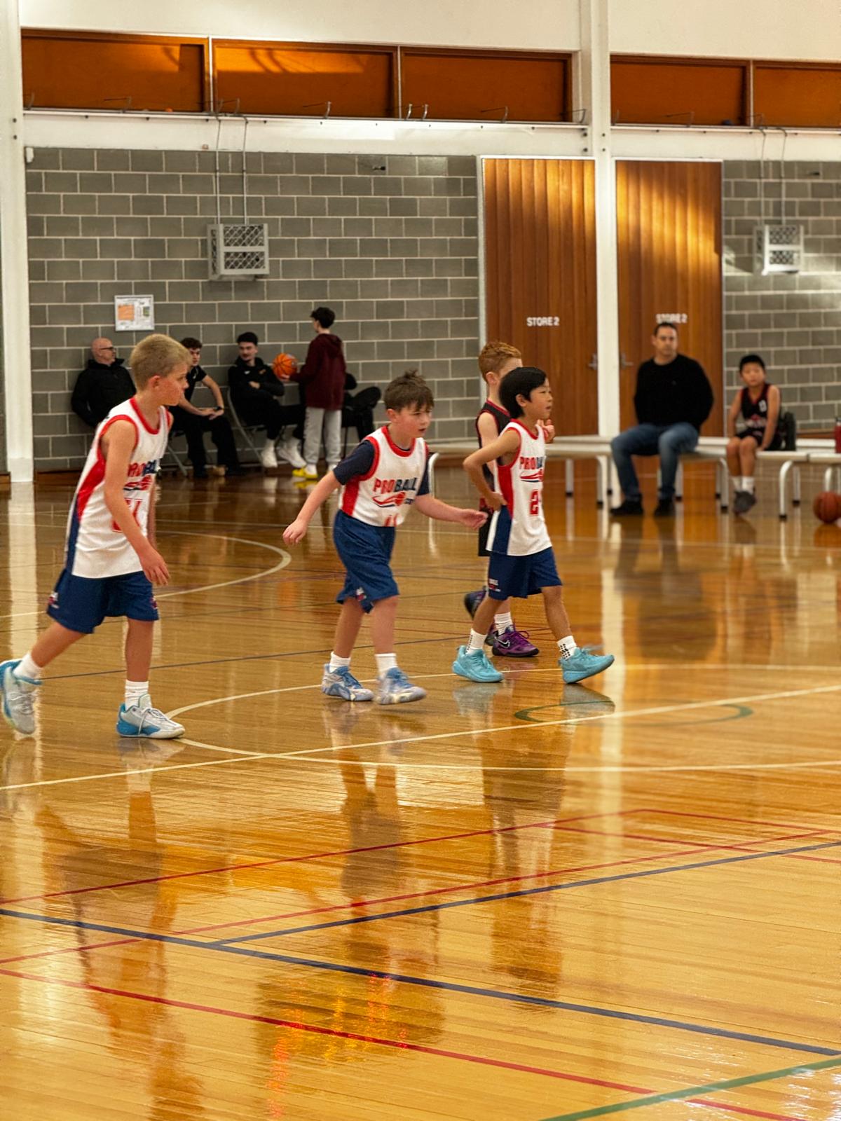 Young basketball player in a ProBall uniform stands confidently on court beside teammates and a coach. Bold headline reads, “Great sports parents don’t raise great athletes. They raise great adults.” The graphic highlights life lessons learned through youth sport, including showing up on time, persevering through challenges, respecting others, focusing on growth, and building character over trophies, with the message: “Better habits. Better people.”